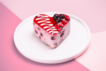 delicious dessert in the shape of a heart, currant cake, cream souffle, decorated with berries and poured jelly on a white plate. On a colored purple background