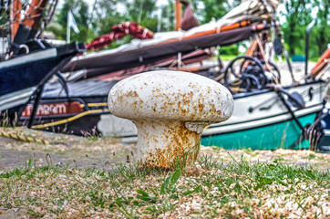 White steel mooring bollard in the port of Hellevoetsluis, The Netherlands, with historic sailing boats in the background