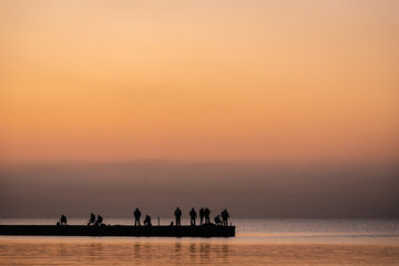 Fototapeta na wymiar Silhouette of people fisherman on pier while beautiful sea sunset or dawn