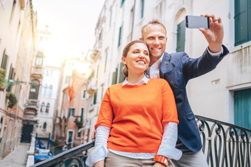 Naklejka premium Szczęśliwa para zakochanych robi selfie na jednym z licznych mostów w Wenecji we Włoszech. Podróż do zdjęcia koncepcyjnego „miasta mostów”.