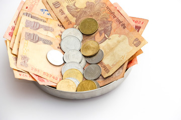 Close up view of donation plate with indian banknotes and coins on white background.
