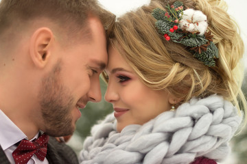 Winter wedding. Couple in love, close-up, heads tilted to each other. A happy woman and a man, the girl has a hairpin in her hair from needles and berries and a snud, a scarf with a large, viscous