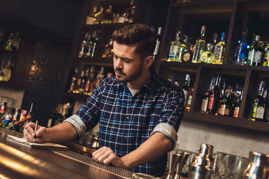 Young Bartender Standing At Bar Counter Writing Receipt Concentrated