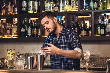 Young bartender standing at bar counter pouring ingredient into shaker concentrated