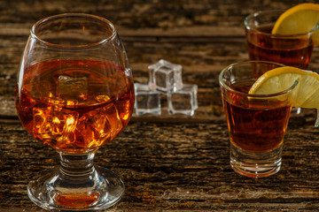 Whiskey with ice or brandy in a glass and a square carafe on an old wooden background. Whiskey with ice in a glass. Whiskey or cognac. Selective focus.