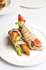 Tortilla sandwich roll with fried fish and vegetables on plate. Red tomato, pickled cucumber and lettuce