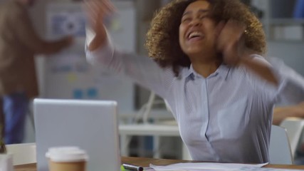 Tracking medium shot of ecstatic young black woman looking at laptop computer and waiting nervously for project results, then screaming and celebrating success