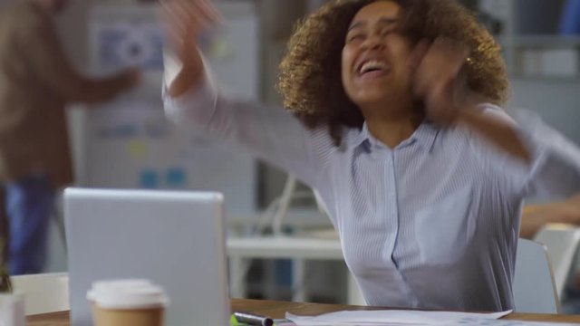 Tracking medium shot of ecstatic young black woman looking at laptop computer and waiting nervously for project results, then screaming and celebrating success