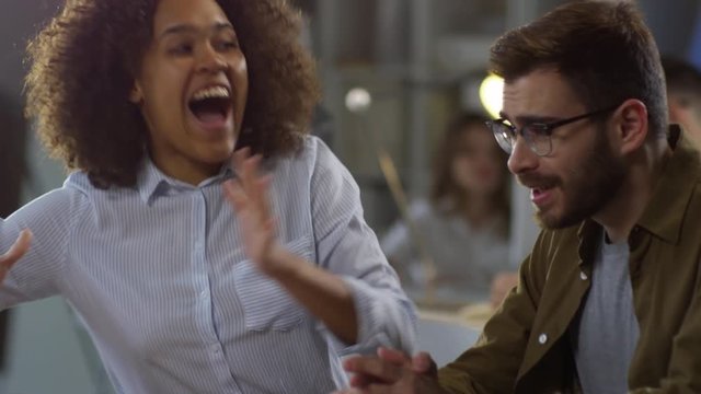 Tracking medium shot of young black woman and bearded Caucasian man high fiving each other when celebrating successful project