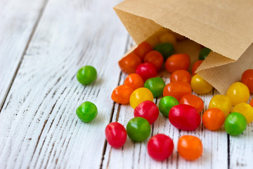 Round colored candy in a paper bag on a wooden table, bright sweets, background