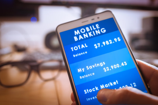 Male hand holdding a smartphone with mobile banking app on screen with blurred office as background