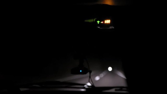 Car rides at night on a very bad road. The car cracks and staggers. Inside view. Dashboard, radio, DVR. Overtaking. Oncoming cars blind eyes. Headlights light the way. Road signs and marking