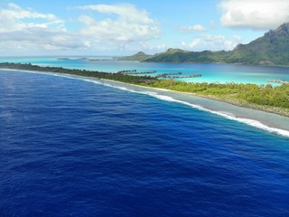 Aerial panoramic landscape view of the island of Bora Bora in French Polynesia with the Mont Otemanu mountain surrounded by a turquoise lagoon, motu atolls, reef barrier, and the South Pacific Ocean - obrazy, fototapety, plakaty
