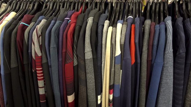 Fashionable collection of warm clothes. Various sweaters hang on hangers on the rack. HD video 