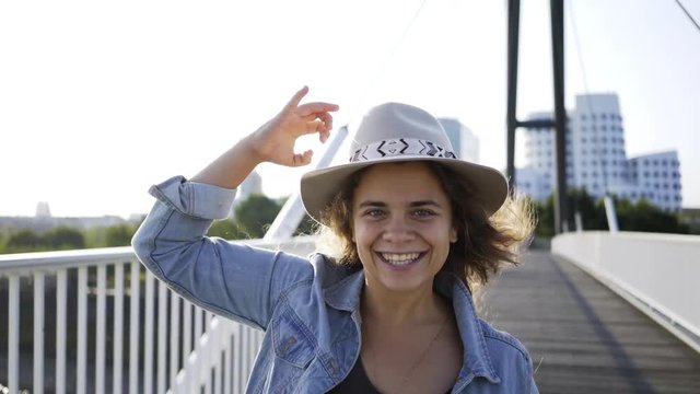 Woman running on modern bridge in sunny morning. Young girl happily smiling, waving hat in hand and to make invitation gesture. POV view woman following for the man Dusseldorf, Germany