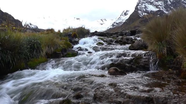 View on a cloudy day of the snowy Huaytapallana next to a small river in the central mountain range of the Peruvian Andes