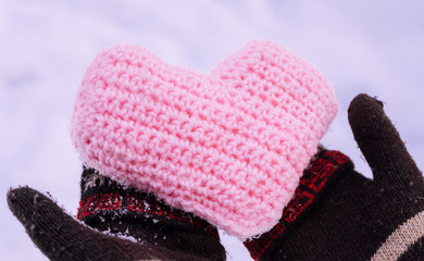 Knitted heart in women's hands wearing winter gloves on snow background