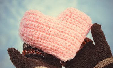 Knitted heart in women's hands wearing winter gloves on snow background