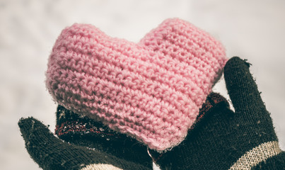 Knitted heart in women's hands wearing winter gloves on snow background