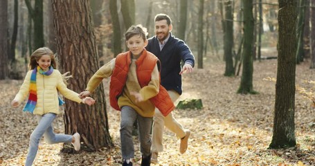 Joyful Caucasian kids, sister and brother, running and having fun in wood with their handsome father. Outdoor.