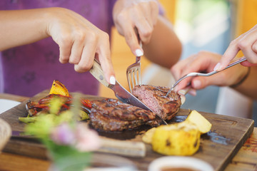 Cooked steak piece of meat on a wooden board with vegetables and potatoes on the table in the restaurant.