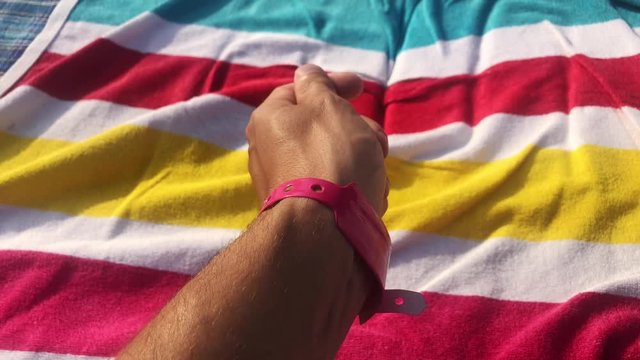 Man with pink bracelet on a hand. Resort or hotel. Person sunbathing at beach towel colourful. LGBT. Unrecognizable people at sunny summer day.