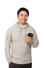 An attractive man in his 20s standing against a white background wearing a grey hood shirt smiling and holding a take-away cup coffee cup, looking at camera.