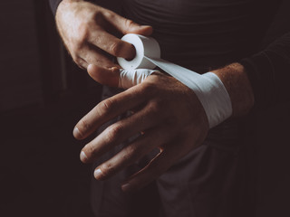 Midsection of man wrapping hand with white boxing wrap