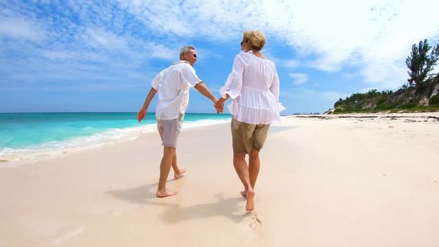 Senior couple walking barefoot on beach vacation Bahamas