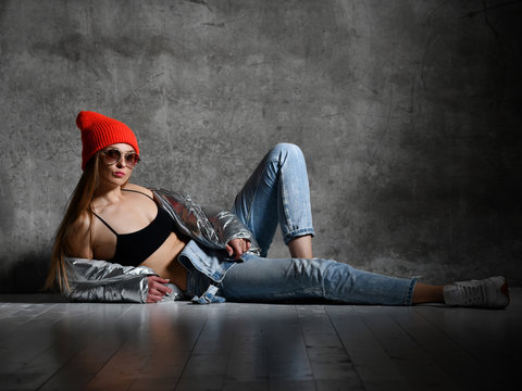 Young sport woman after workout exercise sitting point finger in silver sexy thin down puffer jacket blue jeans red hat 