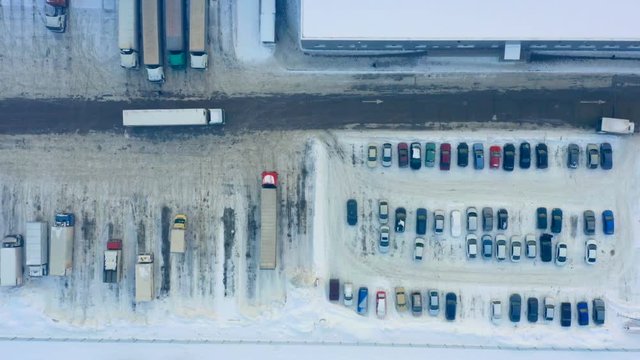 Aerial top view of a semi-trailer truck maneuvers on a snowy parking lot of warehouse logistics dock on a winter day