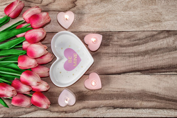 Flowers tulips, a heart-shaped plate and a heart-shaped candle. Festive background to the St. Valentine's Day in pink colors.