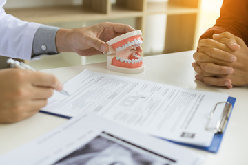 Confident dentist man holding a dentures with talking senior patient at office room.