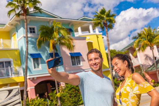 Selfie photo couple tourists taking picture with smart phone in Fort Myers, Florida at colorful wood beach cottages. USA summer travel lifestyle. Asian woman and Caucasian man smiling at mobile phone.