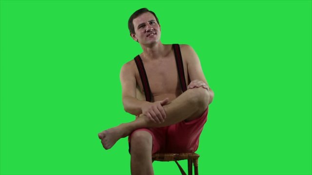  Young sexy man with a beautiful muscular body is resting sitting on a deck chair on green background.  Happy man shirtless posing on camera.