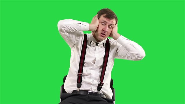 Tired businessman against on green screen. Weary white collar worker after work keeps his head both hands on green background.