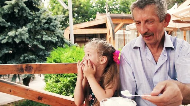 Children with grandfather having dinner in restaurant. Kids with grandfather for dessert eating tasty ice cream at summer cafe. Grandpa is feeding his little grandchildren with ice-cream. 