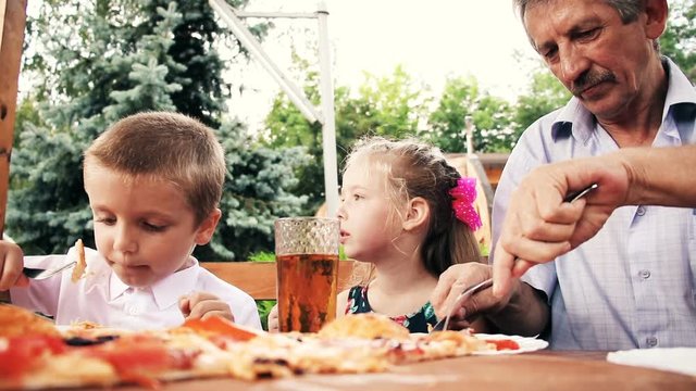 Family having lunch in cafe. Tasty dinner with grandfather. Kids with grandfather for lunch eating tasty pizza at summer cafe. 