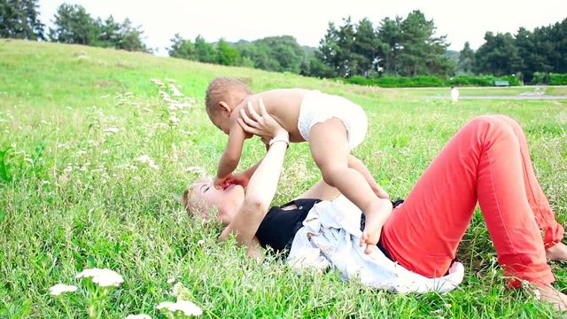 Mom playing with her baby on the grass. Happy multiracial family, mother and her one years old little son vacation in a sunny day in the park. Carefree, fun lifestyle.