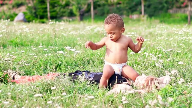 Mom playing with her baby on the grass. Happy multiracial family, mother and her one years old little son vacation in a sunny day in the park.
