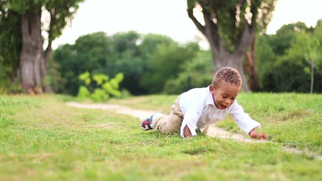 Baby learn to walk. Cute little afro-american boy in a white shirt at sunset plays and crawls on grass in the lawn. Cheerful small boy having fun.