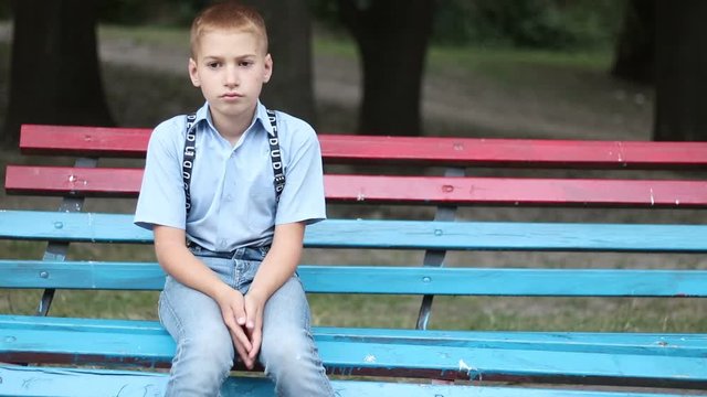 Sad single-boy sitting on a bench in park. Sad, thoughtful,mirthless, lonely mood.