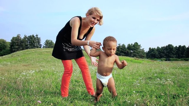 Baby learn to walk. Happy multiracial family. Young mother and her one years old little son for a walk. Baby taking their first steps. 