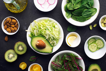 Cooking fresh green salad. Iceberg leaves, spinach, sorrel, cucumbers, radishes, avocados, lemon for a healthy diet. On a dark background. Top view.