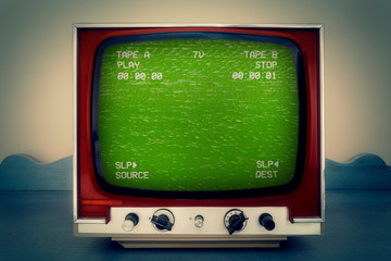 A retro vintage TV showing a green VHS tape screen tracking a noisy signal coming from a double deck. Cool retro vintage backdrop.