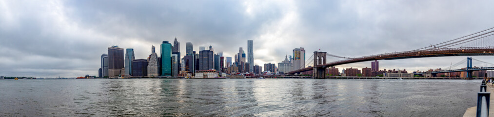 Fototapeta na wymiar Panorama photo of the Brooklyn Bridge and Manhattan with the tops of the skyscrapers reaching the clouds in New York, United States