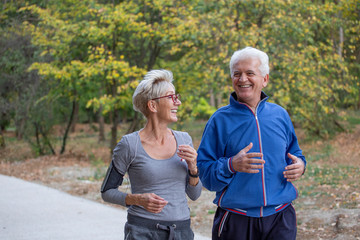 Active senior couple jogging in the park at autumng day and smile