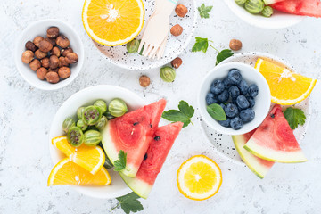 Ingredients of healthy nutrition. Slices of watermelon, blueberries, orange, gooseberries, green berries, nuts, fruit plate. On a light background. Top view.