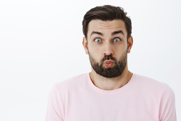 Close-up shot of funny and playful childish cute young dad fooling around playing with kids folding lips and raising eyebrows, popping eyes at camera as aping having fun over gray background