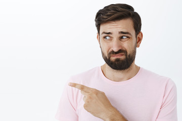 Insecure and timid displeased silly guy with beard smirking looking and pointing left with aversion...